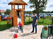 Zwei Kinder rutschen auf einem Kinderspielplatz mit Sand, Klettergerüsten und einer Rutsche